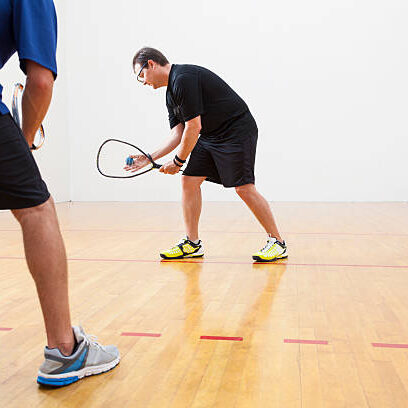 Two men playing racquetball on court. One serving.